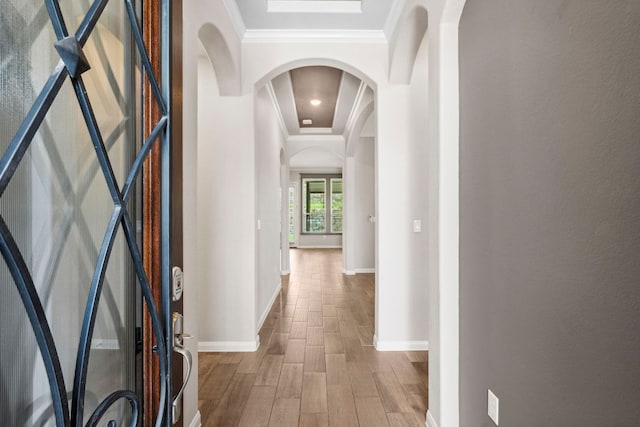 hallway with crown molding, arched walkways, baseboards, and wood finished floors