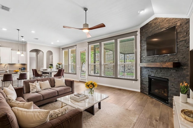 living area with visible vents, a stone fireplace, ceiling fan, light wood-type flooring, and arched walkways