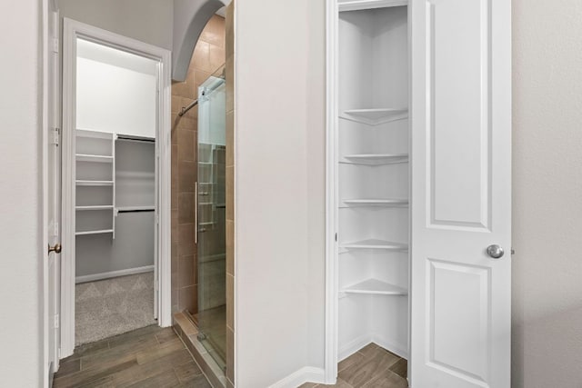 full bathroom with built in features, a shower stall, wood finished floors, and a spacious closet