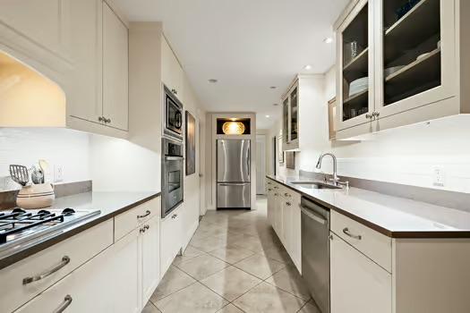 kitchen with glass insert cabinets, white cabinetry, a sink, appliances with stainless steel finishes, and light tile patterned floors