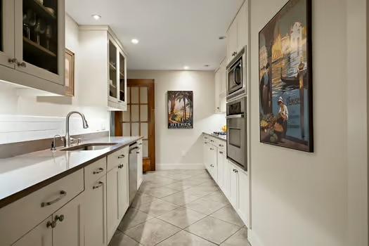 kitchen featuring appliances with stainless steel finishes, a sink, baseboards, glass insert cabinets, and light tile patterned flooring