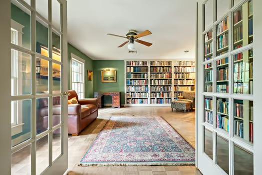 living area featuring ceiling fan, wall of books, and built in shelves