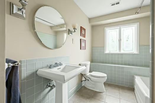 full bathroom with a bathtub, visible vents, tile walls, tile patterned floors, and toilet