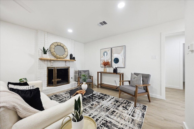 living area featuring visible vents, a brick fireplace, wood finished floors, baseboards, and recessed lighting