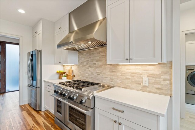 2902 Cedarview Dr, Austin, TX 78704 - kitchen featuring appliances with stainless steel finishes, wall chimney range hood, light wood-style flooring, white cabinets, and recessed lighting