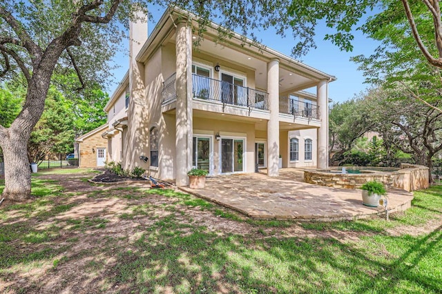 rear view of property with an outdoor hot tub, a chimney, a patio area, a balcony, and stucco siding
