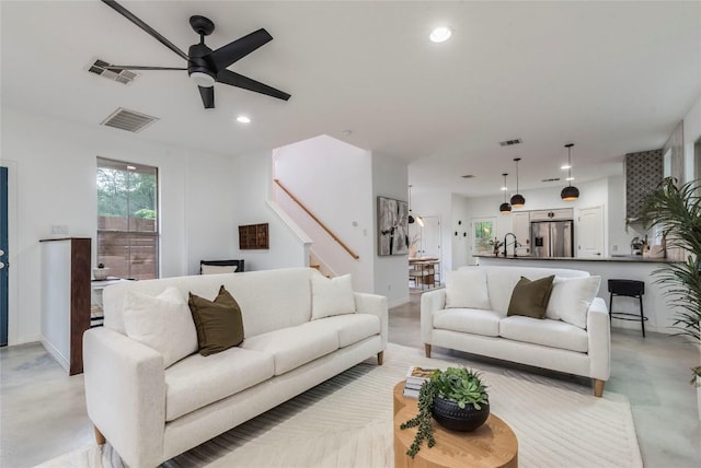 living area with finished concrete flooring, a ceiling fan, stairs, and visible vents
