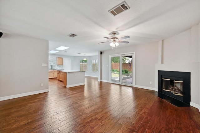 unfurnished living room featuring dark wood-style floors, visible vents, and a fireplace with flush hearth