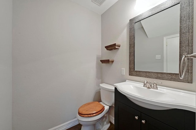 half bathroom featuring vanity, baseboards, toilet, and visible vents