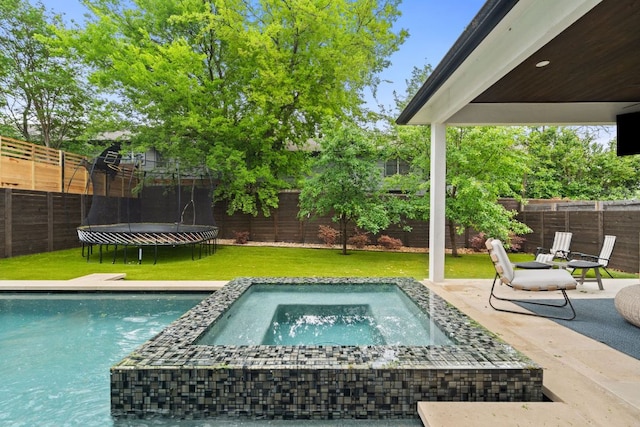 view of swimming pool featuring a lawn, a fenced backyard, a trampoline, and an in ground hot tub