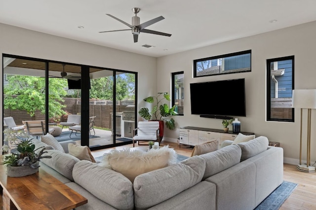 living room with visible vents, a ceiling fan, light wood finished floors, and baseboards