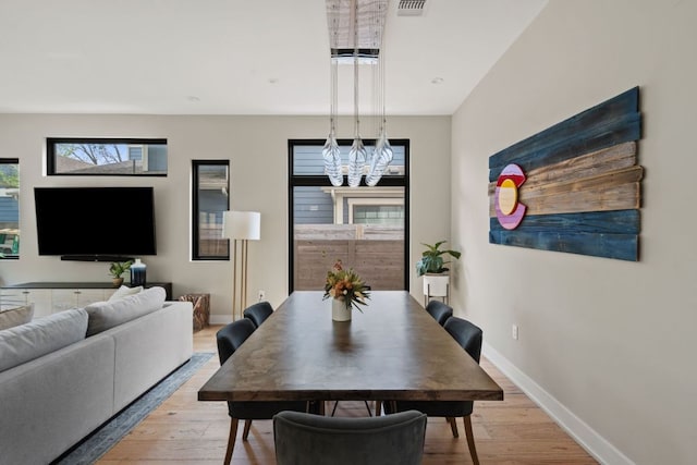 dining space with baseboards, light wood finished floors, a notable chandelier, and visible vents