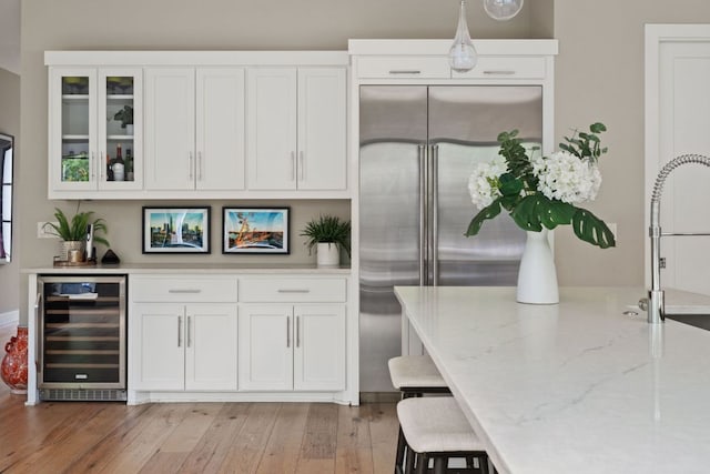 kitchen with beverage cooler, built in refrigerator, light wood-style floors, and white cabinetry