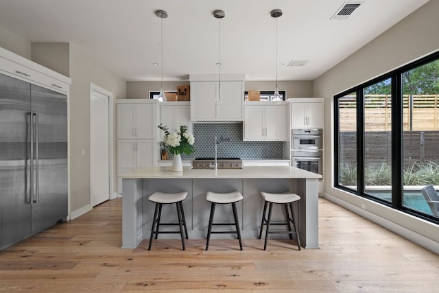 kitchen with decorative backsplash, visible vents, appliances with stainless steel finishes, light countertops, and light wood-style floors