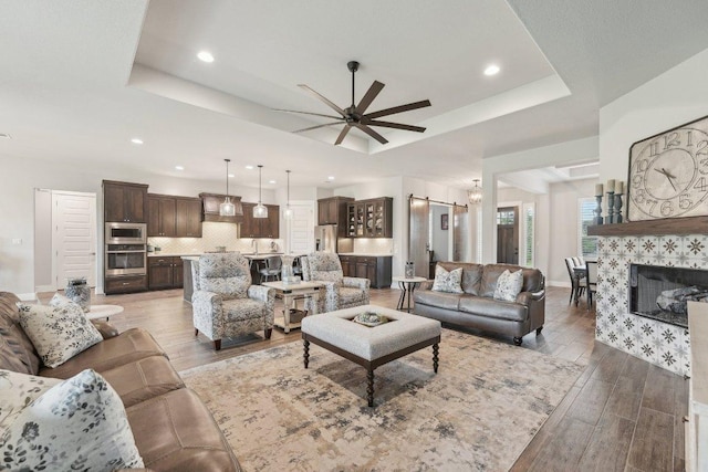 living area with recessed lighting, ceiling fan, wood finished floors, and a tray ceiling