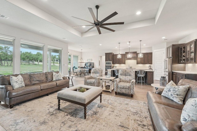 living area featuring a ceiling fan, visible vents, a healthy amount of sunlight, and a raised ceiling