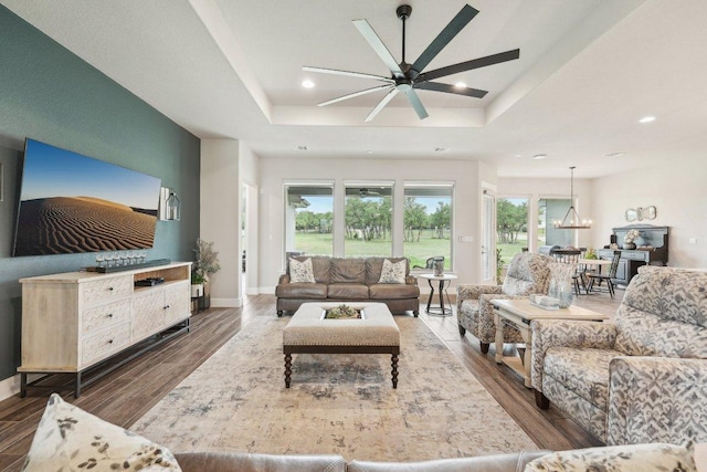 living area with a healthy amount of sunlight, a raised ceiling, ceiling fan with notable chandelier, and wood finished floors