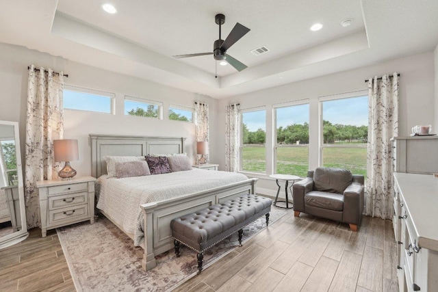 bedroom with visible vents, light wood-style floors, a tray ceiling, and multiple windows