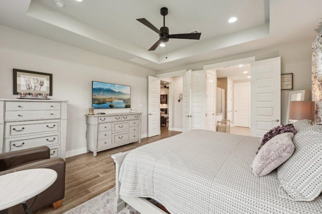 bedroom featuring baseboards, a tray ceiling, recessed lighting, and wood finished floors