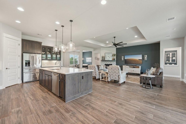 kitchen featuring appliances with stainless steel finishes, dark brown cabinets, a sink, open floor plan, and a tray ceiling