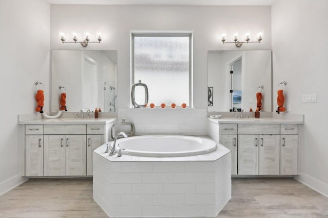 full bathroom featuring a garden tub, two vanities, and wood finished floors