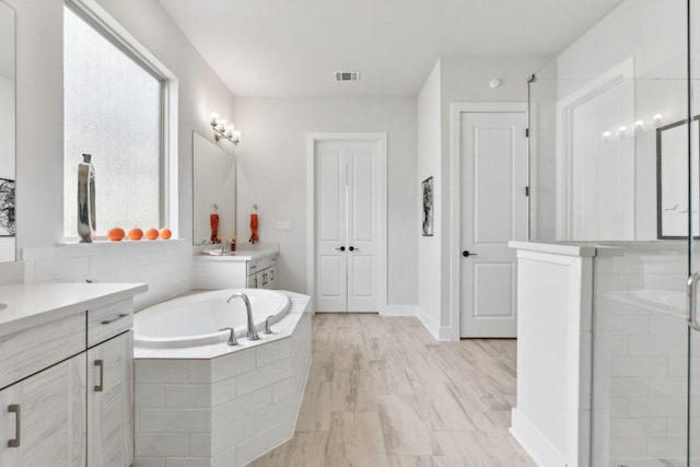 bathroom featuring visible vents, a garden tub, two vanities, and a shower stall