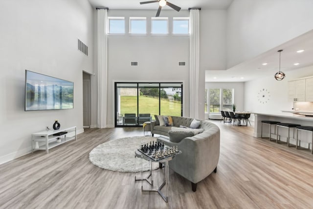 living room with a high ceiling, a ceiling fan, wood finished floors, and visible vents
