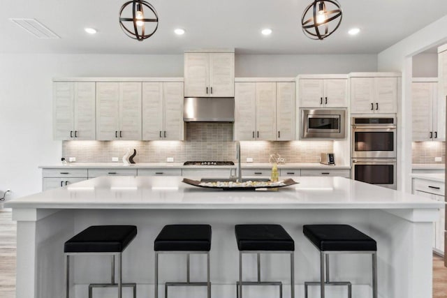 kitchen with light countertops, under cabinet range hood, a sink, backsplash, and stainless steel appliances