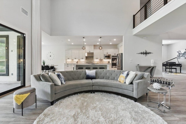 living room with recessed lighting, light wood-style floors, visible vents, and a towering ceiling