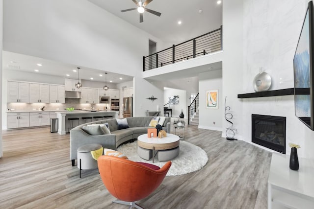 living room featuring stairway, a high ceiling, a ceiling fan, and light wood-style flooring