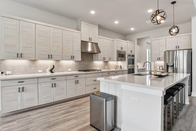 kitchen with a kitchen bar, tasteful backsplash, under cabinet range hood, light wood-style floors, and stainless steel appliances