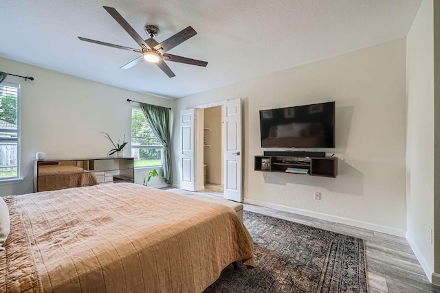 bedroom featuring baseboards, ceiling fan, wood finished floors, and multiple windows