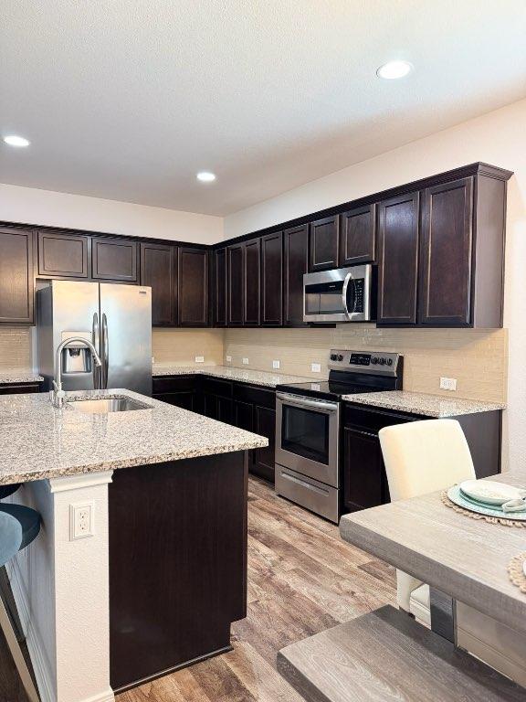 1045 Gaelic Dr, Georgetown, TX 78626 - kitchen with stainless steel appliances, light wood-type flooring, light stone counters, dark brown cabinets, and recessed lighting
