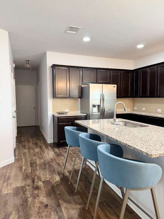 kitchen with visible vents, dark wood-style floors, a kitchen bar, stainless steel fridge with ice dispenser, and a sink