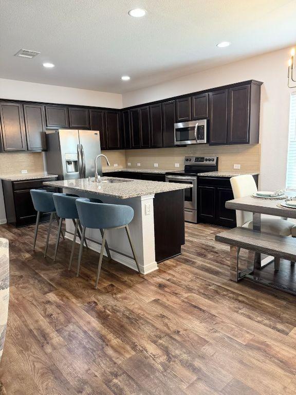 1045 Gaelic Dr, Georgetown, TX 78626 - kitchen with appliances with stainless steel finishes, an island with sink, dark wood-type flooring, tasteful backsplash, and recessed lighting