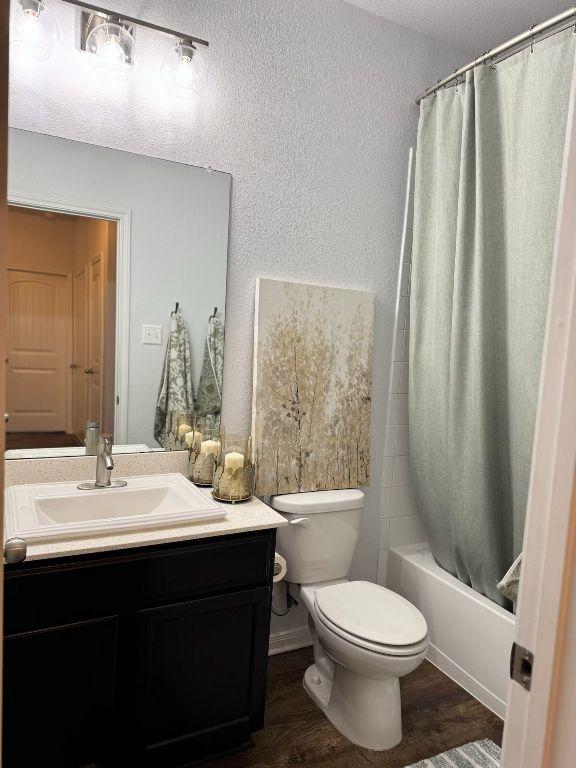 full bathroom featuring vanity, a textured wall, wood finished floors, toilet, and shower / bath combo