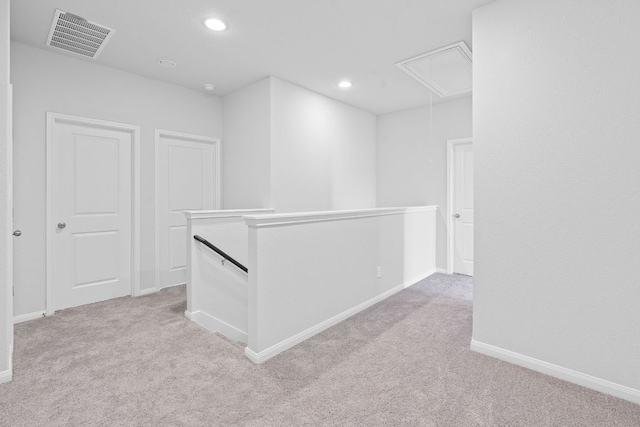 hallway with visible vents, attic access, an upstairs landing, and light colored carpet