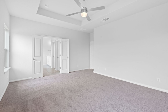 unfurnished bedroom featuring carpet floors, a tray ceiling, visible vents, and baseboards