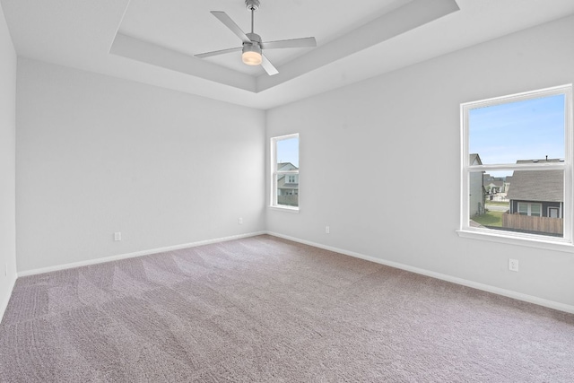 empty room with baseboards, a ceiling fan, a raised ceiling, and carpet