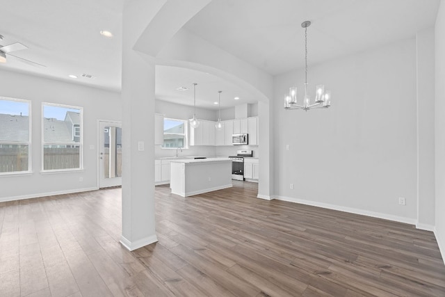 unfurnished living room featuring a sink, arched walkways, recessed lighting, baseboards, and dark wood-style floors