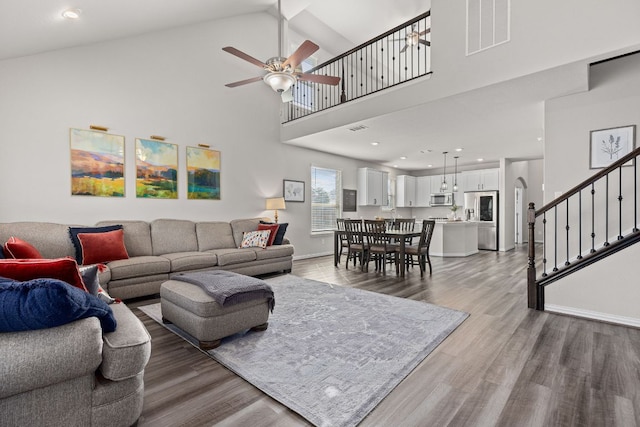 living room with visible vents, stairs, a towering ceiling, wood finished floors, and ceiling fan
