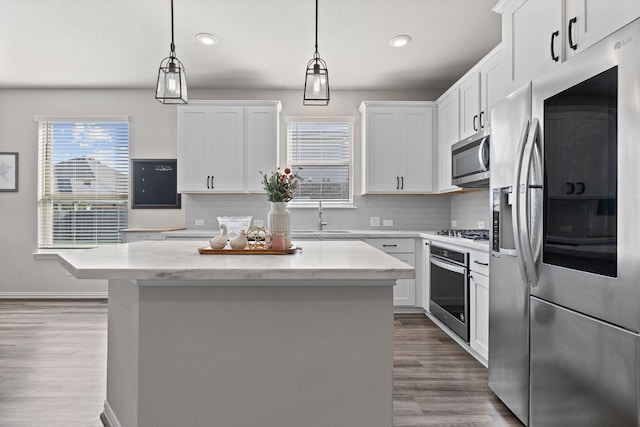 kitchen featuring appliances with stainless steel finishes, a sink, backsplash, wood finished floors, and a kitchen island