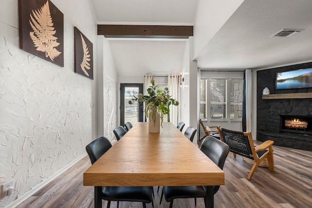 dining space with a textured wall, a fireplace, baseboards, wood finished floors, and visible vents