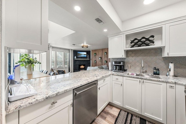 kitchen featuring backsplash, visible vents, stainless steel dishwasher, a sink, and a warm lit fireplace