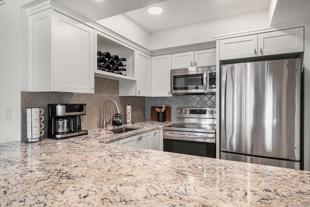 kitchen featuring decorative backsplash, light stone countertops, a sink, white cabinets, and stainless steel appliances