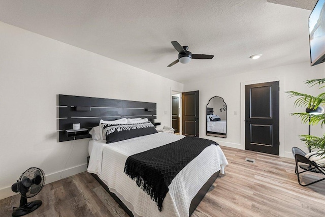 bedroom with ceiling fan, a textured ceiling, visible vents, baseboards, and light wood finished floors
