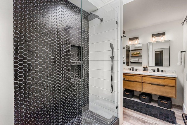 full bathroom featuring double vanity, a sink, walk in shower, and wood finished floors