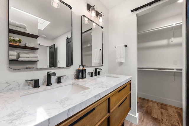 full bath with double vanity, a sink, wood finished floors, and a spacious closet