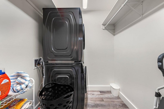 laundry area featuring baseboards, laundry area, wood finished floors, and stacked washer and clothes dryer