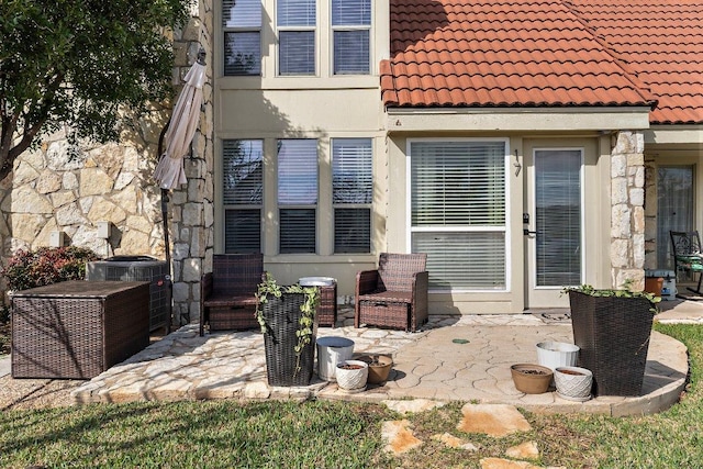 rear view of property with a tile roof, stone siding, stucco siding, a patio area, and central air condition unit